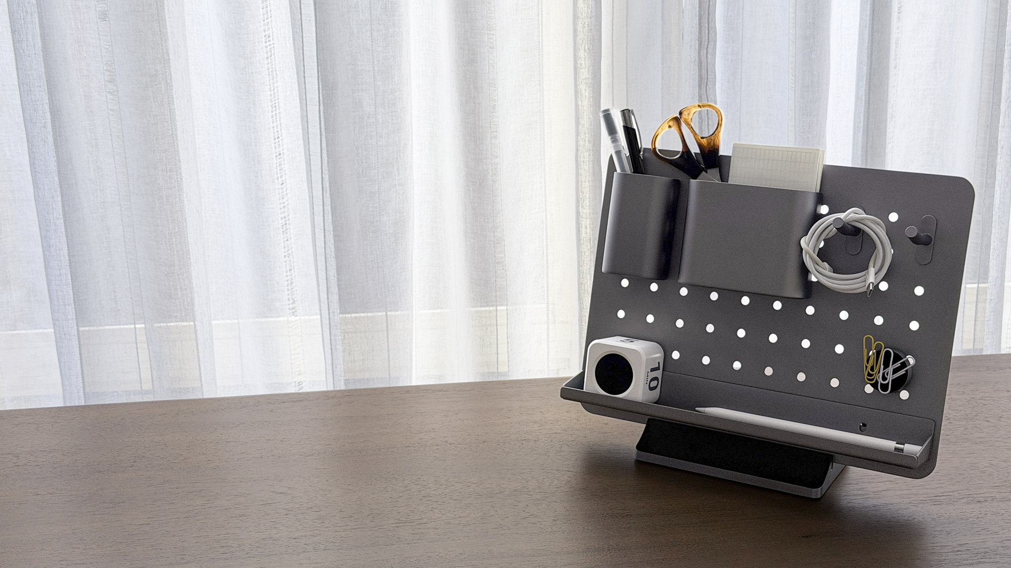 Desk organizer with stationery items on a wooden surface with white curtains in the background