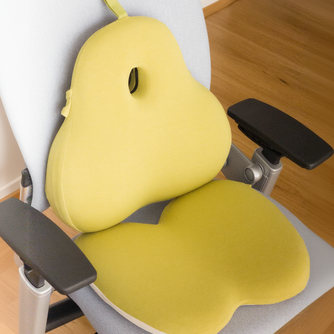 Yellow ergonomic seat cushion on a chair with a wooden floor background