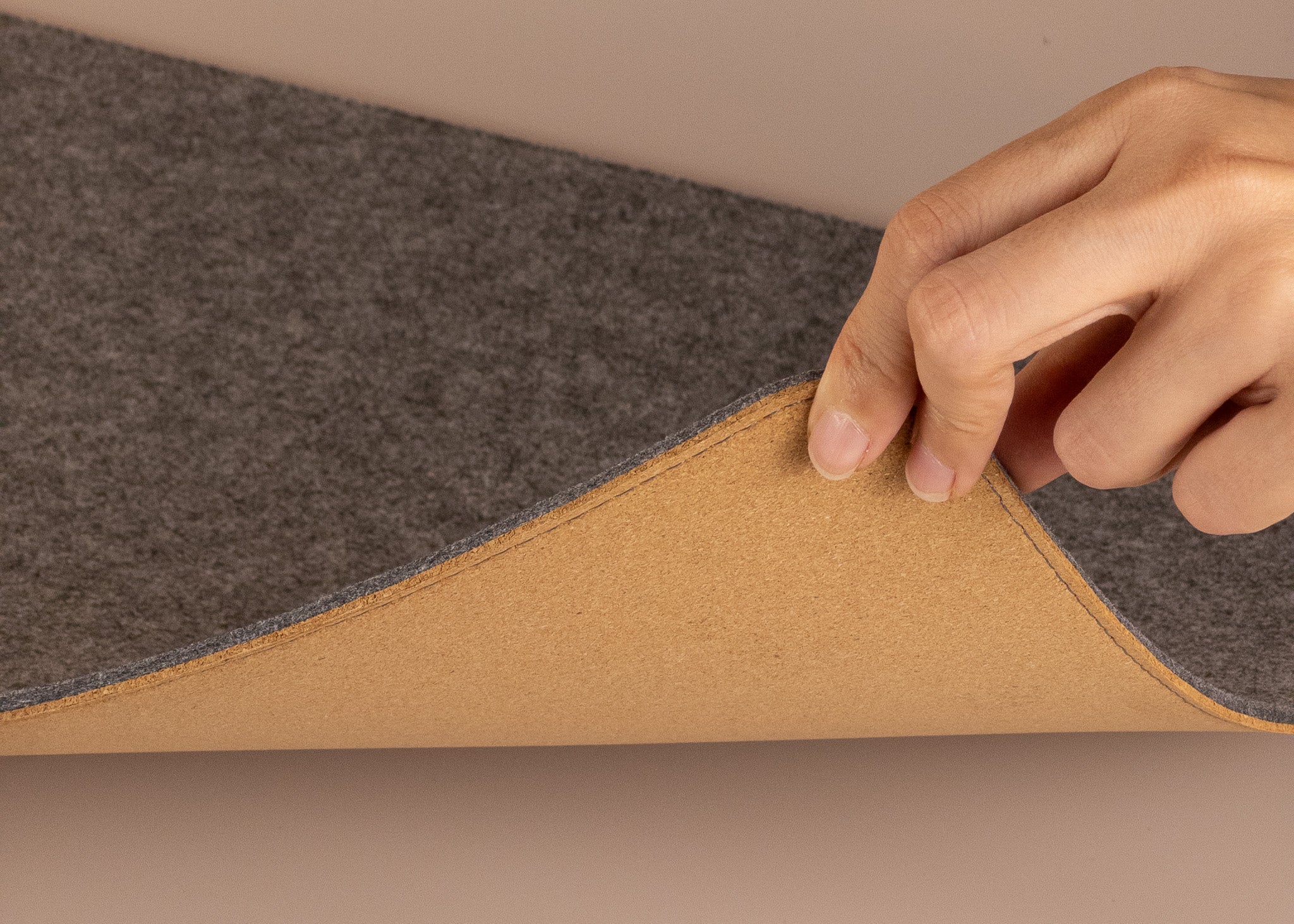 Hand lifting grey felt and cork desk mat to show natural cork backside, flexible and durable