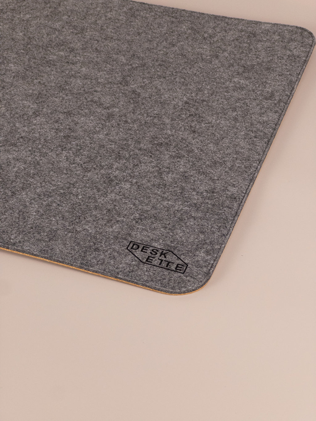 Close-up of Deskette logo on felt and cork desk mat, minimalist design