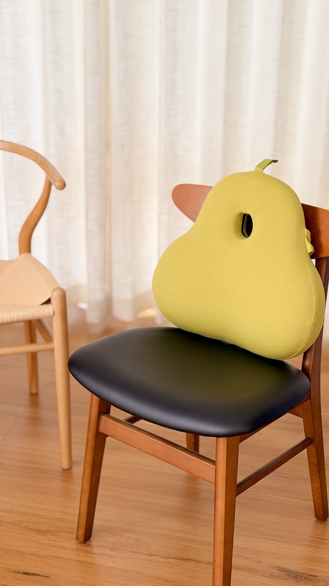 Yellow pear-shaped cushion on a chair with a light curtain background