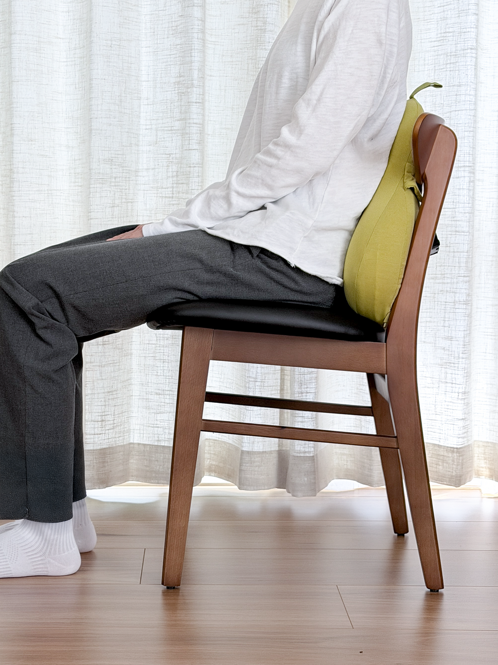 Person sitting on a wooden chair with a yellow bag over their shoulder, wearing a white shirt and dark pants.