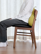 Person sitting on a wooden chair with a yellow bag over their shoulder, wearing a white shirt and dark pants.