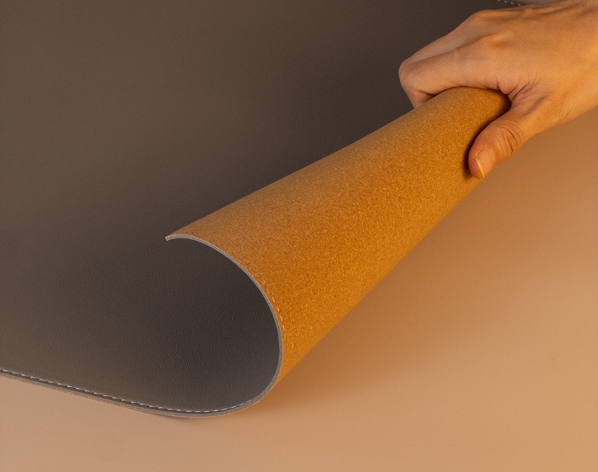 Hand lifting slim grey leather desk mat to show natural cork backside, flexible and durable design