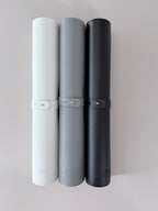 Rolled up slim leather desk mats in white, grey, and black with straps, compact and portable for storage