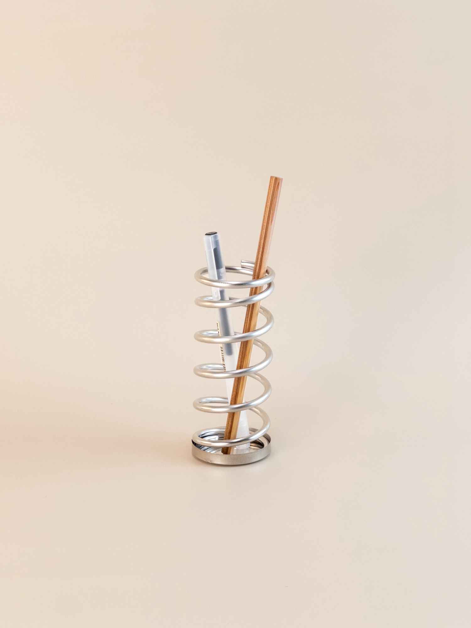 Metallic spiral straw holder with two pens on a beige background