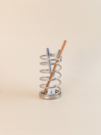 Metallic spiral holder with three pens on a beige background