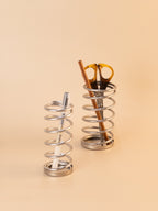 Two metal spiral holders with a pen and scissors on a beige background